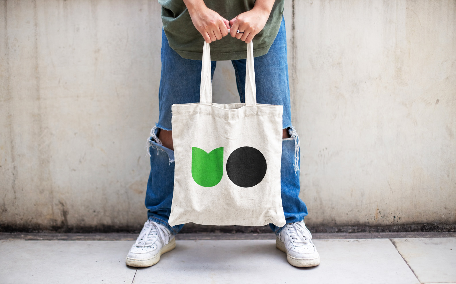 A person holding a canvas tote bag printed with the Urban Optimists logo